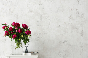 Vase with peonies, magazines and aroma sticks on coffee table near beige grunge wall