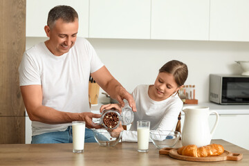 Little girl with her father eating corn balls and drinking milk at table in kitchen