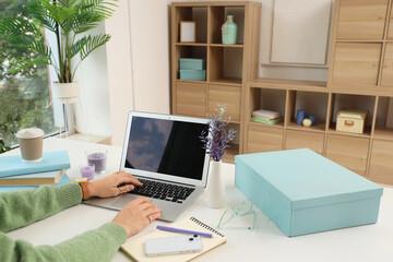 Fototapeta premium Woman's hands typing on laptop keyboard at modern home office desk with coffee, books, and decorative items