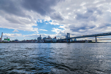 View of Brooklyn Bridge over East River with city skyline and cloudy sky in background. New York. USA.
