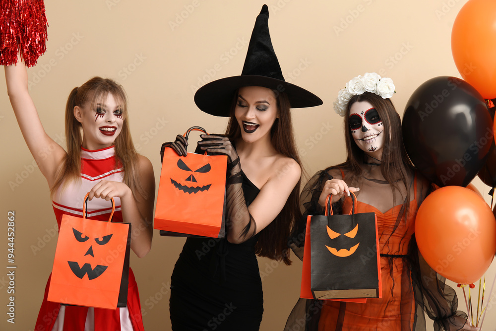 Wall mural Female friends dressed for Halloween with gift bags and balloons on beige background