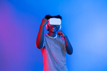 Smiling African American woman with VR headset playing boxing game turning to metaverse at vibrant blue and pink stadium portrait neon lighting in gaming technology interface 3D graphic. Contrivance.