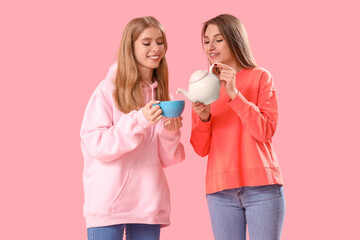 Beautiful young women pouring tea into cup on pink background