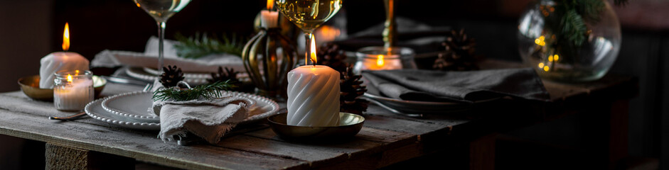 Banner. Beautiful table setting for family Christmas dinner at home. Cozy atmosphere, candlelight. Wine glasses, vintage chandelier, elegant interior. Fir tree branches, wooden furniture, dark, bokeh