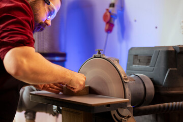 Manufacturer shaping wooden bowl on disc sander in assembling shop. Woodworking expert working in joinery, guiding wood against professional grinding machine rotating disc