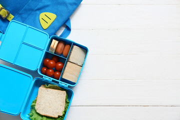 Lunch box with tasty food and school backpack on white wooden background