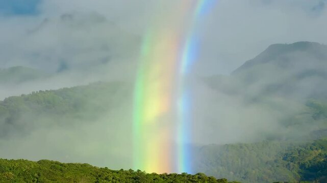 Animation of mountains with colorful rainbow in cloudy sky over field. Nature landscape after storm. Spring morning. St Patrick Day holiday symbol