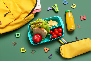 Lunch box with tasty food, school stationery and backpack on chalkboard