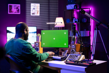 Artist plays midi controller synthesizer next to greenscreen layout, working on producing new music with his audio musical instruments in home studio. Musician using isolated copyspace.