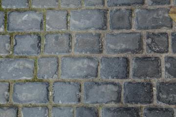 Dark cobble stones . Closeup texture of an old stoneblock pavement cobbled with square granite blocks as an old-fashioned architectural, background .