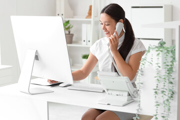 Young female receptionist at workplace talking with phone in office