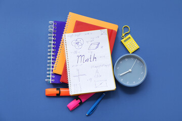 Notebook with calculator, alarm clock and school stationery on blue background