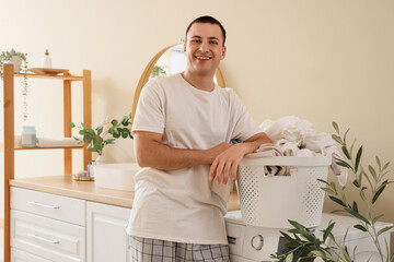 Young man holding basket with dirty clothes in laundry room