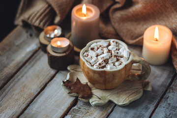 Spicy sweet fall hot drink: delicious pumpkin latte with cinnamon, marshmallow with salted caramel. Served in handmade artisan mug in shape of pumpkins, cozy home decor with candles, dry autumn leaves
