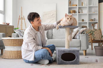 Handsome young happy man and cute Maine Coon cat lying on scratching post at home