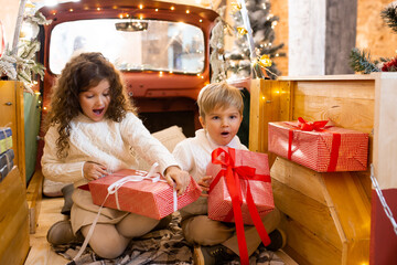 Cute little children boy and girl in pickup trailer with lights on background. Merry Christmas and...
