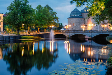 Fototapeta premium Illuminated Orebro Castle and stone bridge in blue hour . Tourist atraction and history entusiast destination. Orebro, Sweden. Copy space