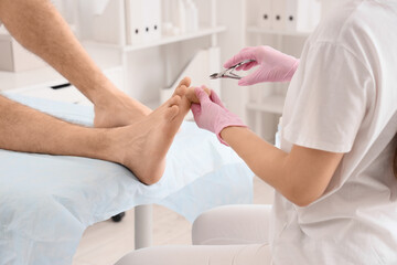 Beautician cutting cuticle off feet of young man on couch in spa salon, closeup