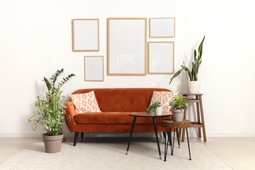 Interior of modern living room with orange sofa and houseplants near white wall