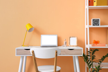 Comfortable workspace with modern laptop near orange wall
