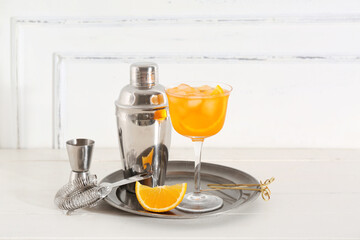 Glass of Aperol spritz cocktail and shaker on white wooden table