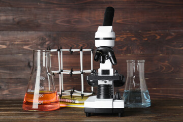 Modern microscope with chemical flasks and molecular model on table against wooden background