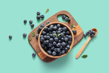 Wooden cutting board and bowl with fresh ripe blueberry on turquoise background