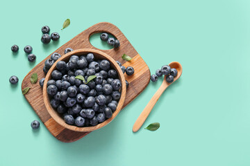 Wooden cutting board and bowl with fresh ripe blueberry on turquoise background