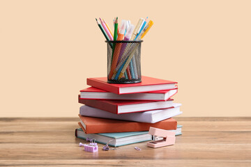Fototapeta premium Stack of books and different stationery on wooden table against color wall