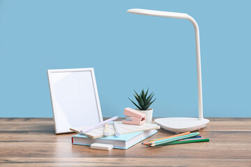 Set of stationery, lamp and blank picture frame on wooden table against color wall