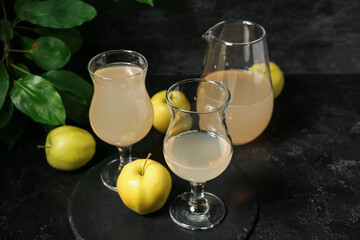 Glasses and jug of fresh apple kvass on black background