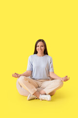 Young woman meditating on beanbag against yellow background