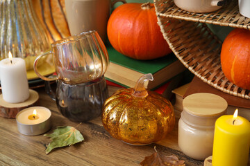 Cups with pumpkins, autumn leaves and burning candles on counter, closeup
