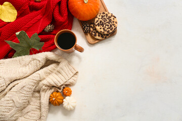 Composition with warm sweaters, cup of coffee, cookies and autumn decor on light background