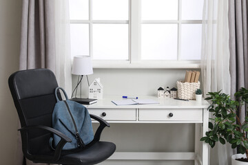 Student's workplace with lamp, house figures and notebooks near window in room