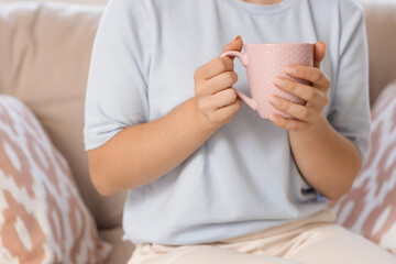 Young woman with cup of tea sitting on sofa at home, closeup