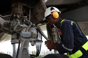The black male aircraft mechanics use hand tools to work on inspection and do maintenance of an...