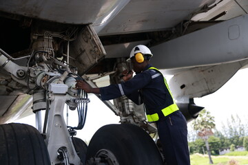 The black male aircraft mechanics use hand tools to work on inspection and do maintenance of an...