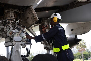 The black male aircraft mechanics use hand tools to work on inspection and do maintenance of an...