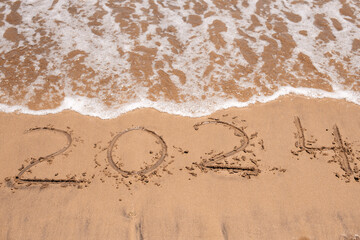 2024 written on the sandy beach, with waves gently rolling in, representing the arrival of a new year full of potential.