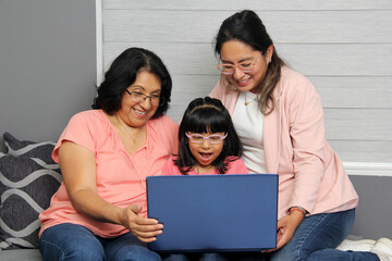 Three generations brunette latina grandmother, mom and daughter with glasses are surprised and excited while using laptop to shop with discounts and promotions