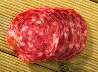 Thin salchichon sausage slices on wooden background, view from above