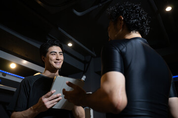 トレーニングジムでタブレットを持って教えるトレーナー　顧客に教えるパーソナルトレーナーやインストラクターのイメージ