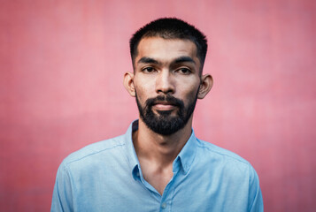 Portrait of handsome bearded Asian man wearing blue shirt on pink background and look at camera