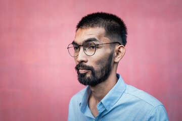 Portrait of handsome bearded Asian man wearing glasses and shirt on pink background.