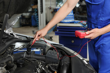 Auto mechanic with multimeter doing diagnostic at automobile repair shop, closeup