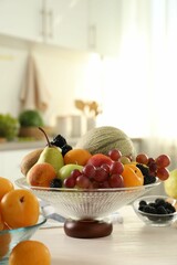 Glass vase with different fruits and berries on white table indoors