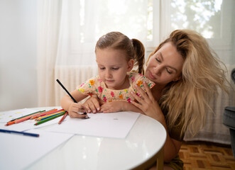 Mother and little daughter drawing together at home 