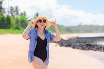 A joyful woman in her 60s enjoying a sunny beach day, feeling confident and beautiful, challenging aging stereotypes. The background features a beach with coconut trees.