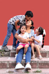 Young Latina mom with 2 daughters and a son show their love with kisses and hugs to celebrate Mother's Day